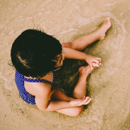 A little girl enjoying the ocean, sitting on the sand. Building an Ecosystem for Ageless Societies.